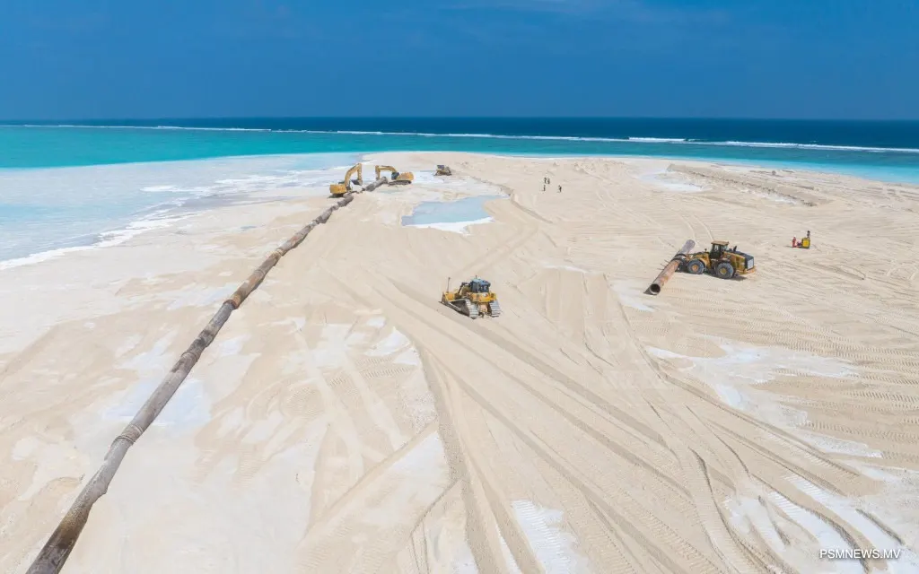 A long sand pipeline and bulldozers on a wide expanse of newly reclaimed land at Ras Malé, with the open sea on the horizon