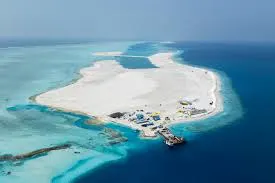 An excavator levelling newly reclaimed white sand at Ras Malé under a pale sky