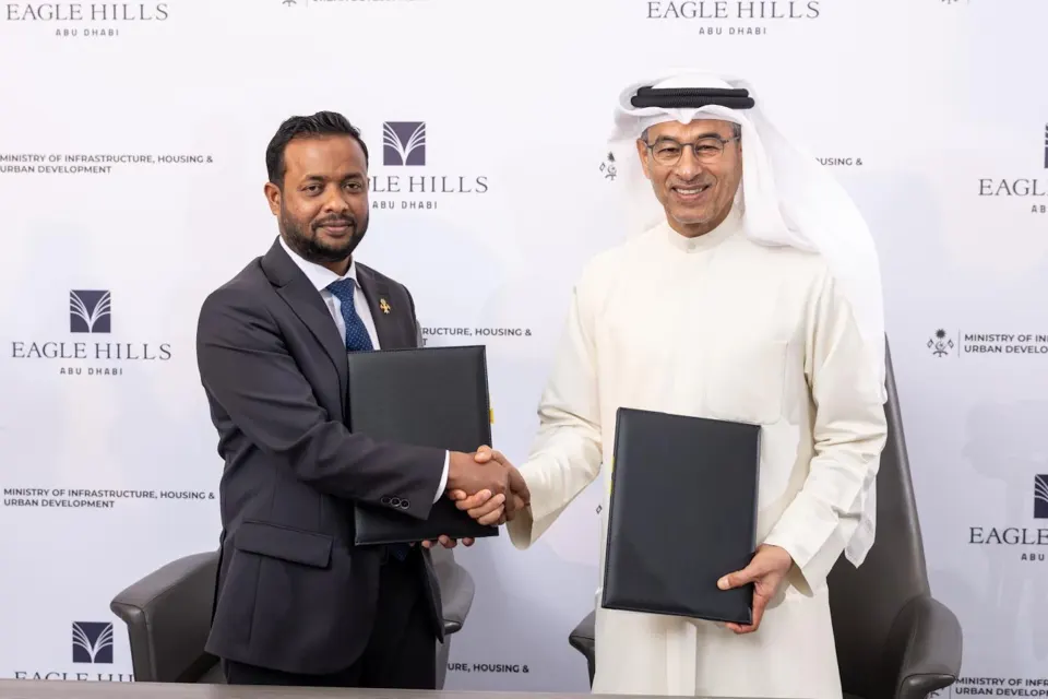 A Maldivian government official and an Eagle Hills representative shake hands in front of branded backdrops at the signing of the Ras Malé waterfront agreement